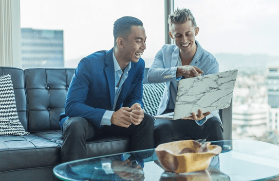 Two Men Sitting On A Couch Looking At A Laptop